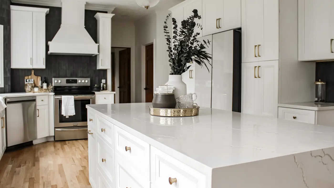 A kitchen with a white island, white cabinets, and brown floors